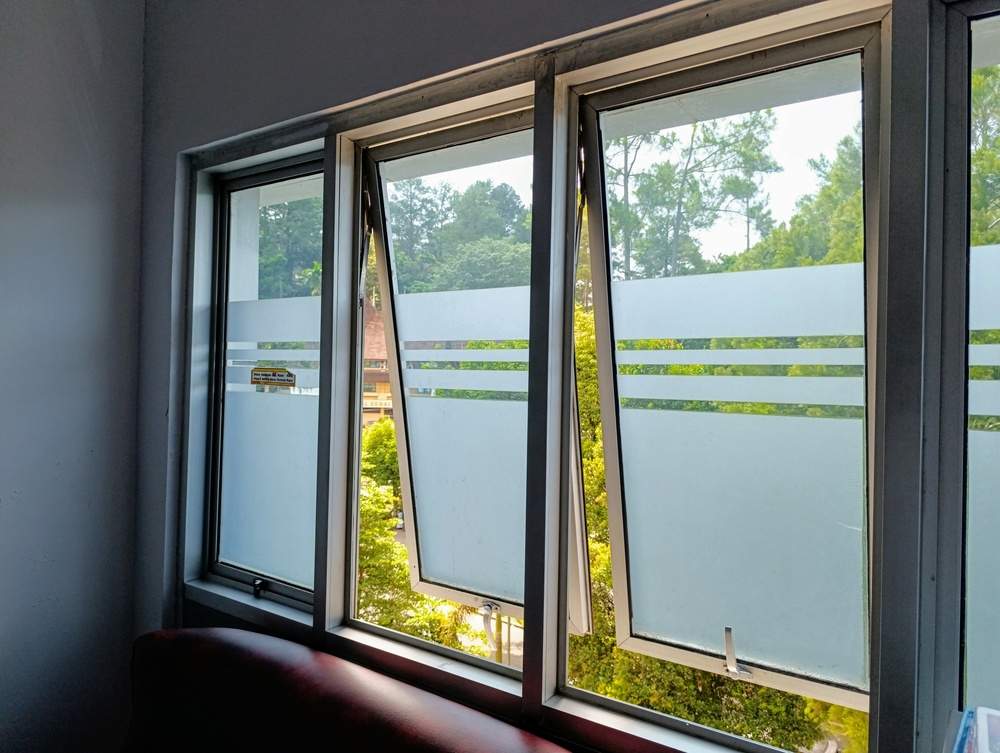 Modern glass windows with frosted privacy patterns, offering a serene view of lush green trees and a sunny outdoor landscape. Ideal for office or home design inspiration