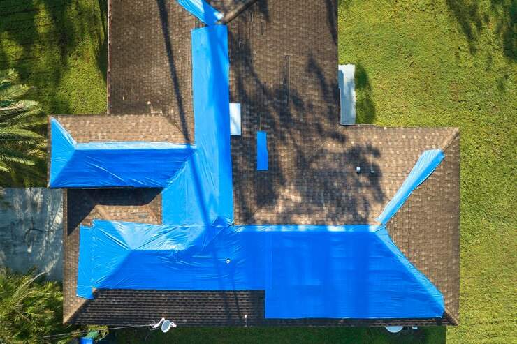 top view leaking house roof covered with protective tarp sheets against rain water leaks until replacement asphalt shingles damage building rooftop